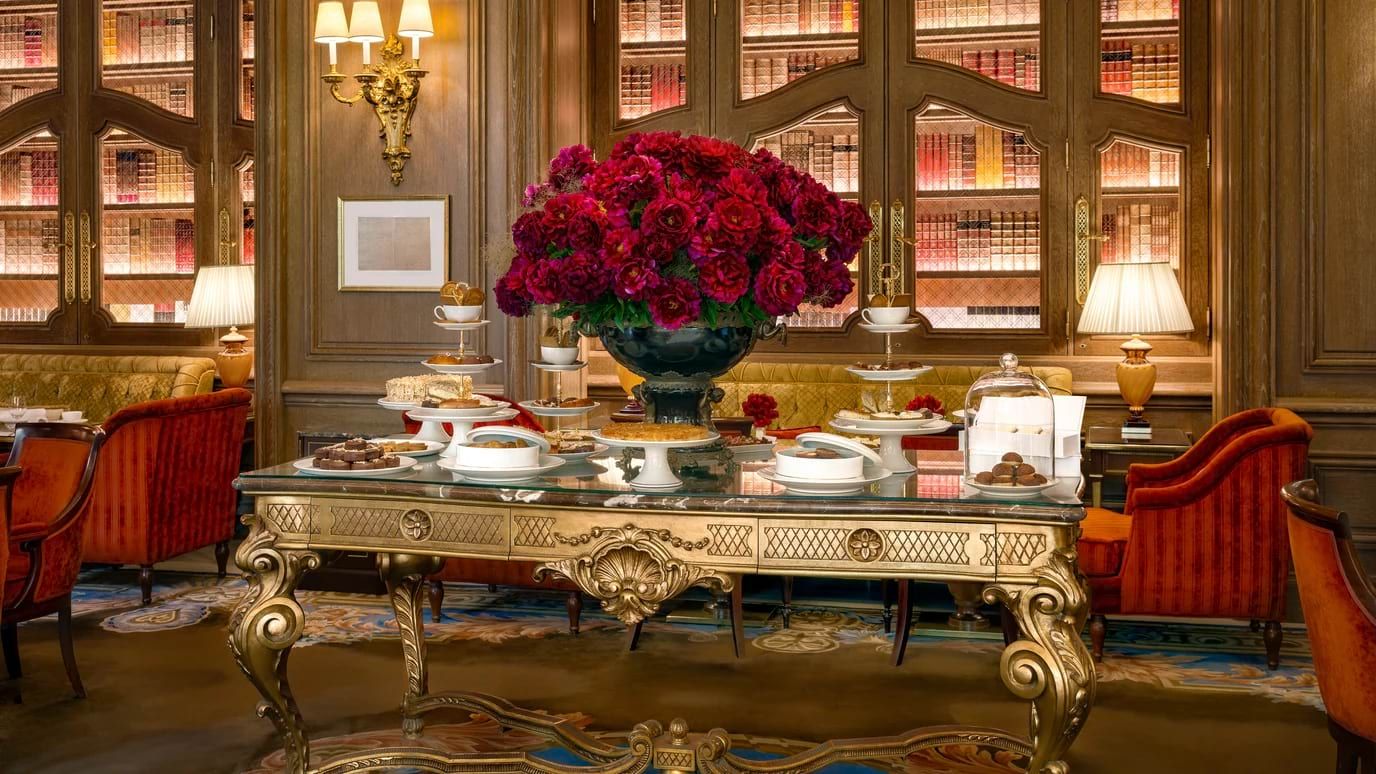Luxury Parisian tea setup on a gold table with scones and vibrant red roses arranged in a decorative vase