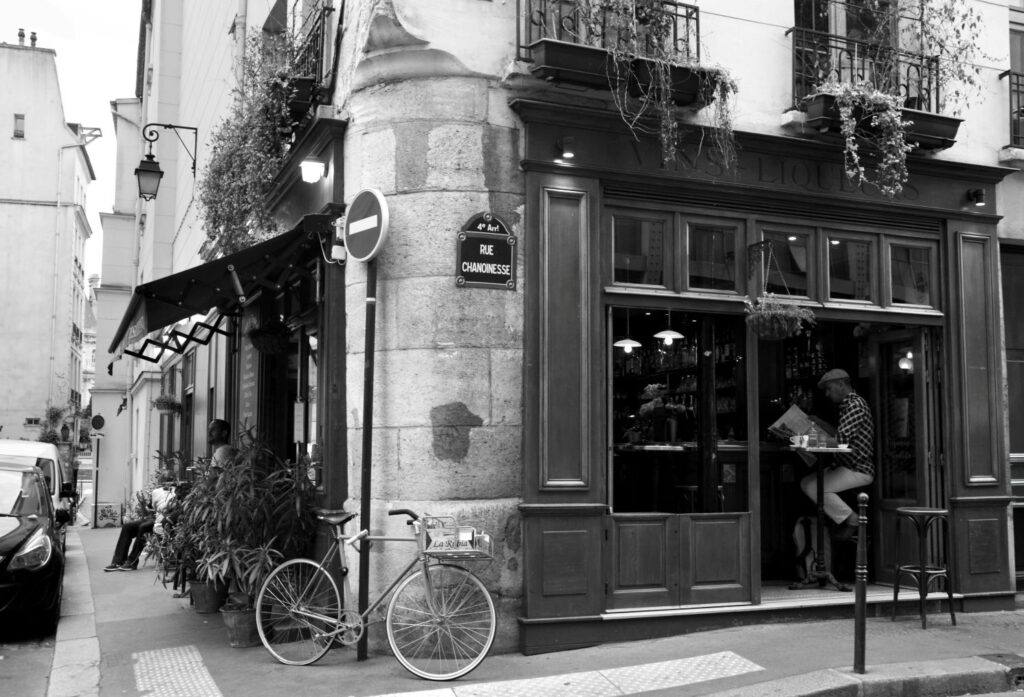 Black-and-white photograph of a Paris café terrace in the early 1900s with patrons enjoying coffee
