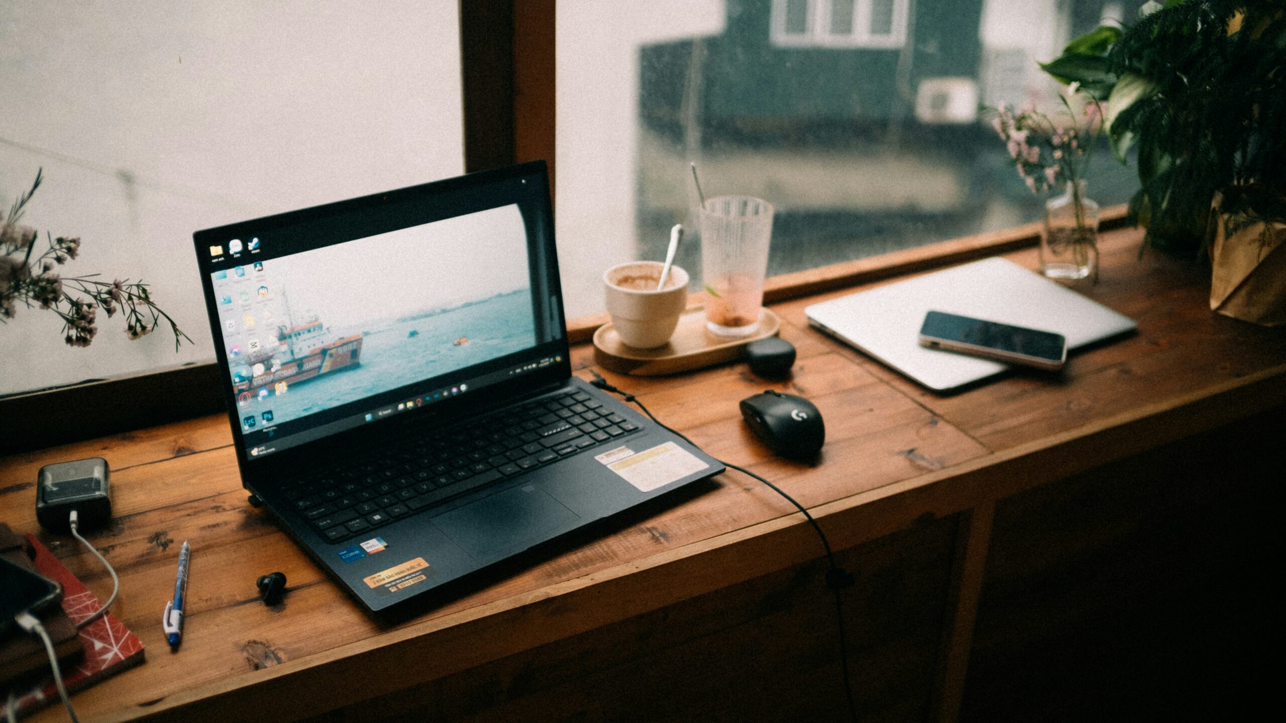 Laptop and coffee on a wooden cafe table by a rain-streaked window while planning a trip online